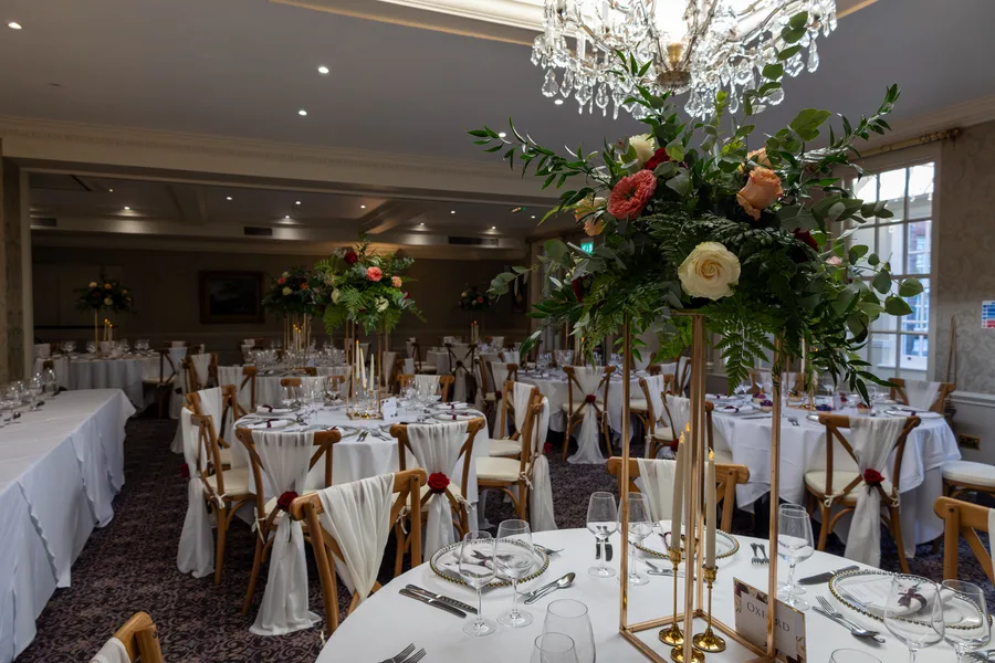 Wedding breakfast room laid with tall floral centrepieces beneath a chandelier