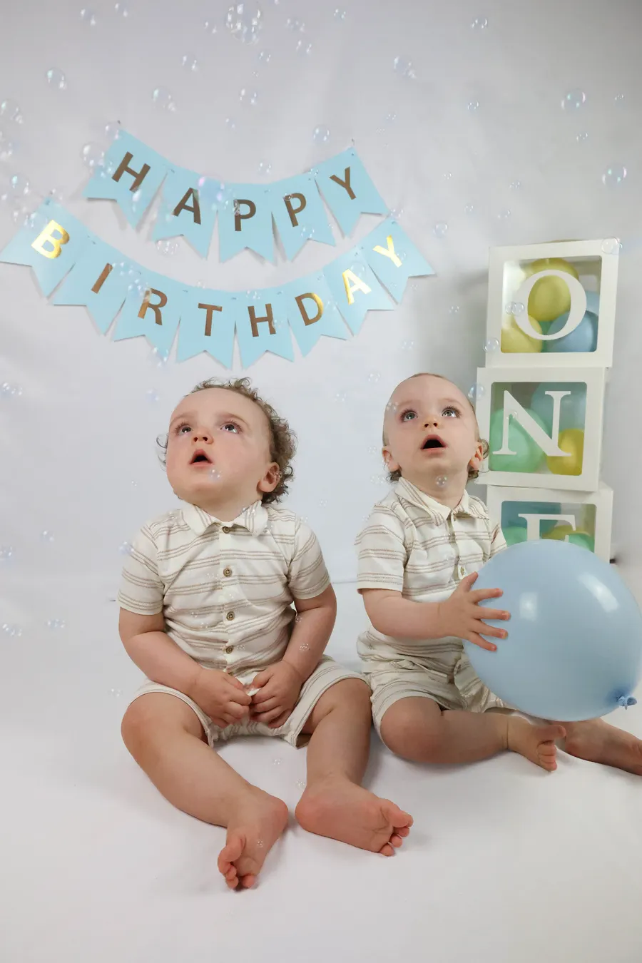 Two one-year-old boys at a first birthday session with a Happy Birthday banner