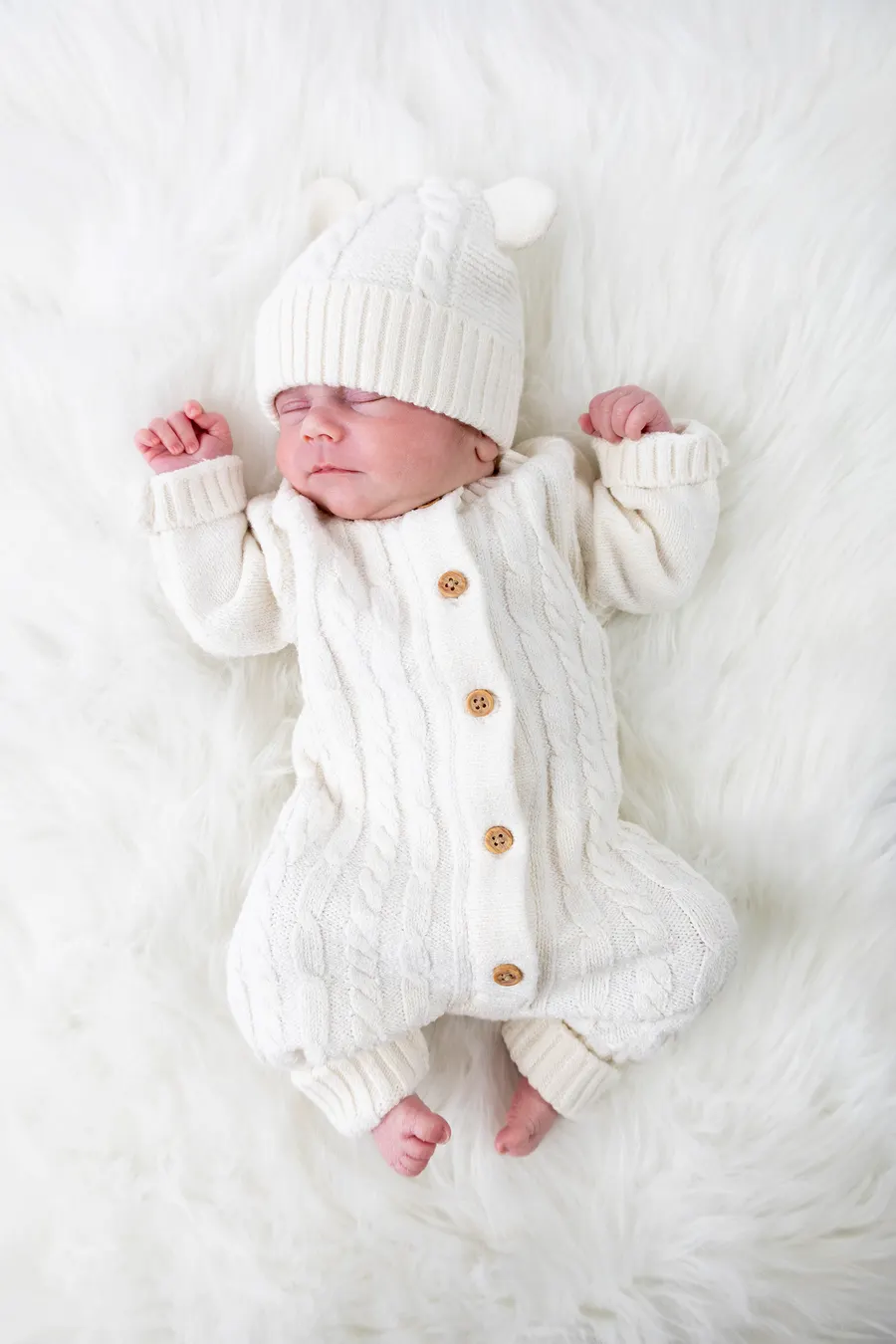 Newborn in a cream knitted romper and bear-ear hat on a fluffy rug