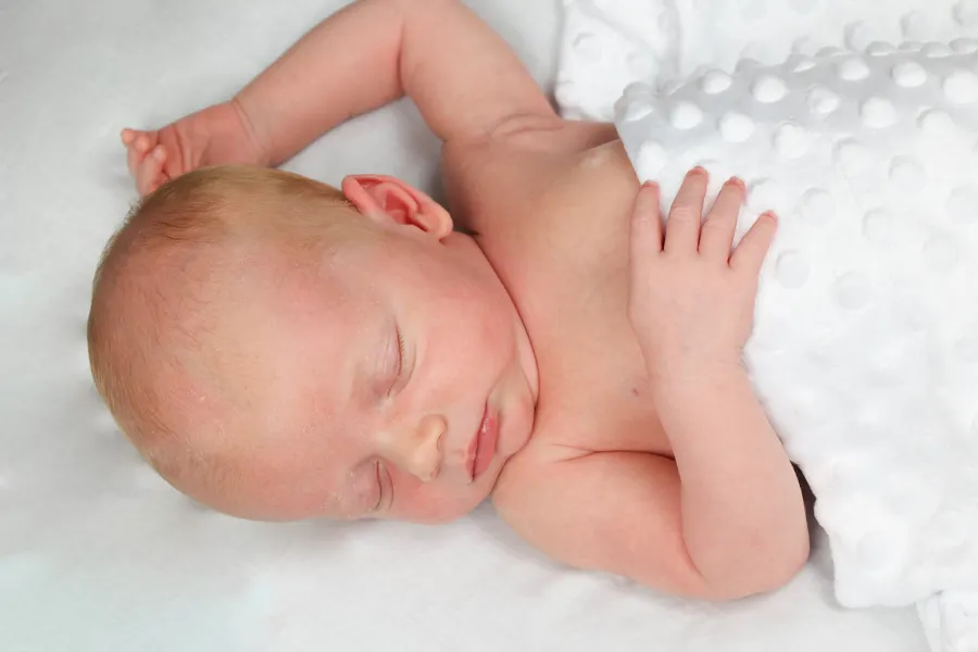 Newborn stretching in their sleep on a white blanket