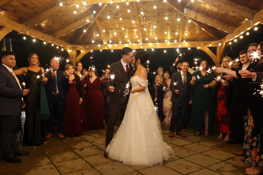 Guests holding sparklers around the couple under a fairy-lit pergola
