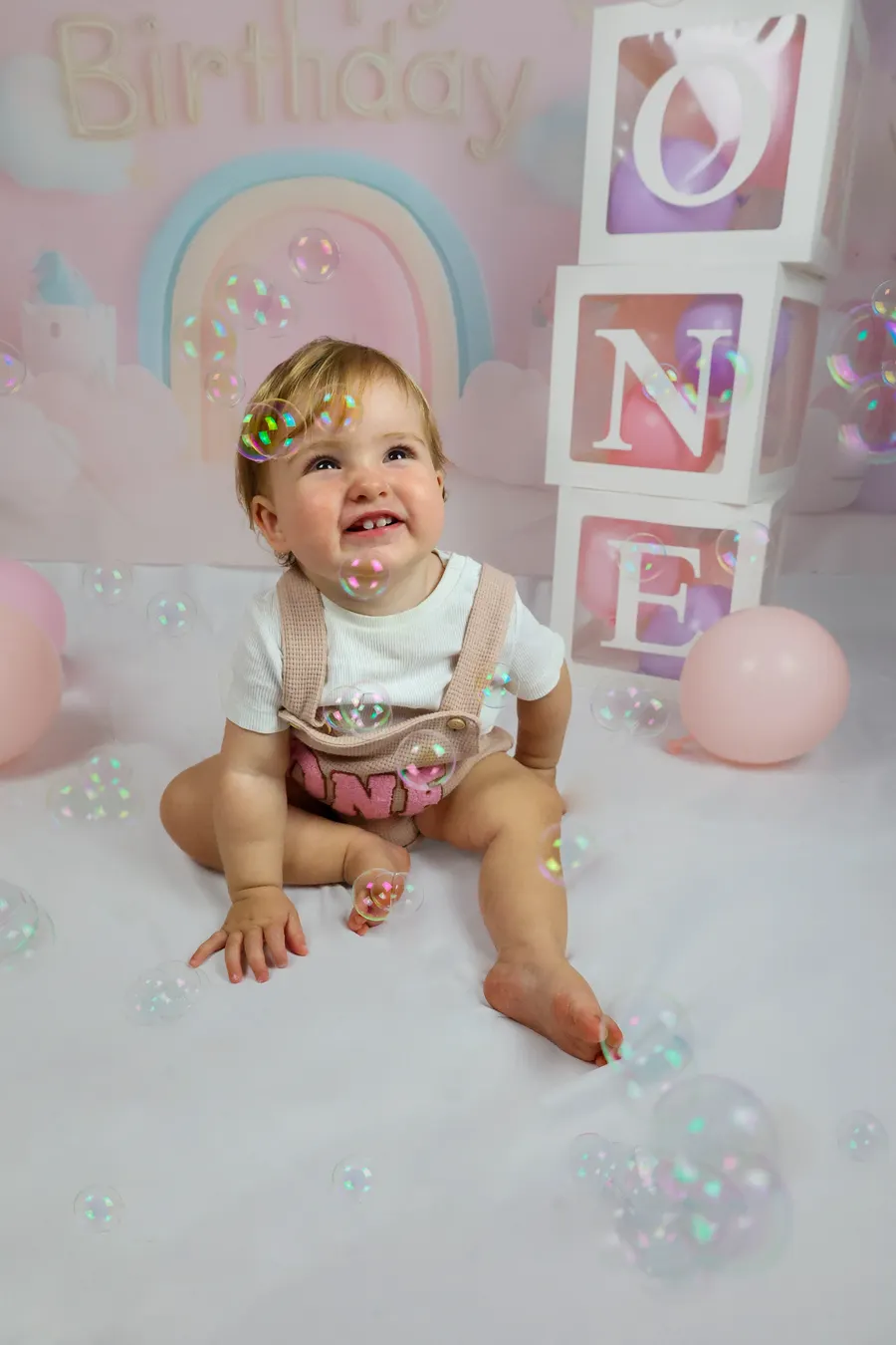 One-year-old girl laughing among bubbles at her pastel first birthday session