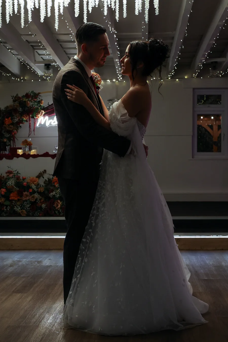 Bride and groom holding each other beneath fairy lights