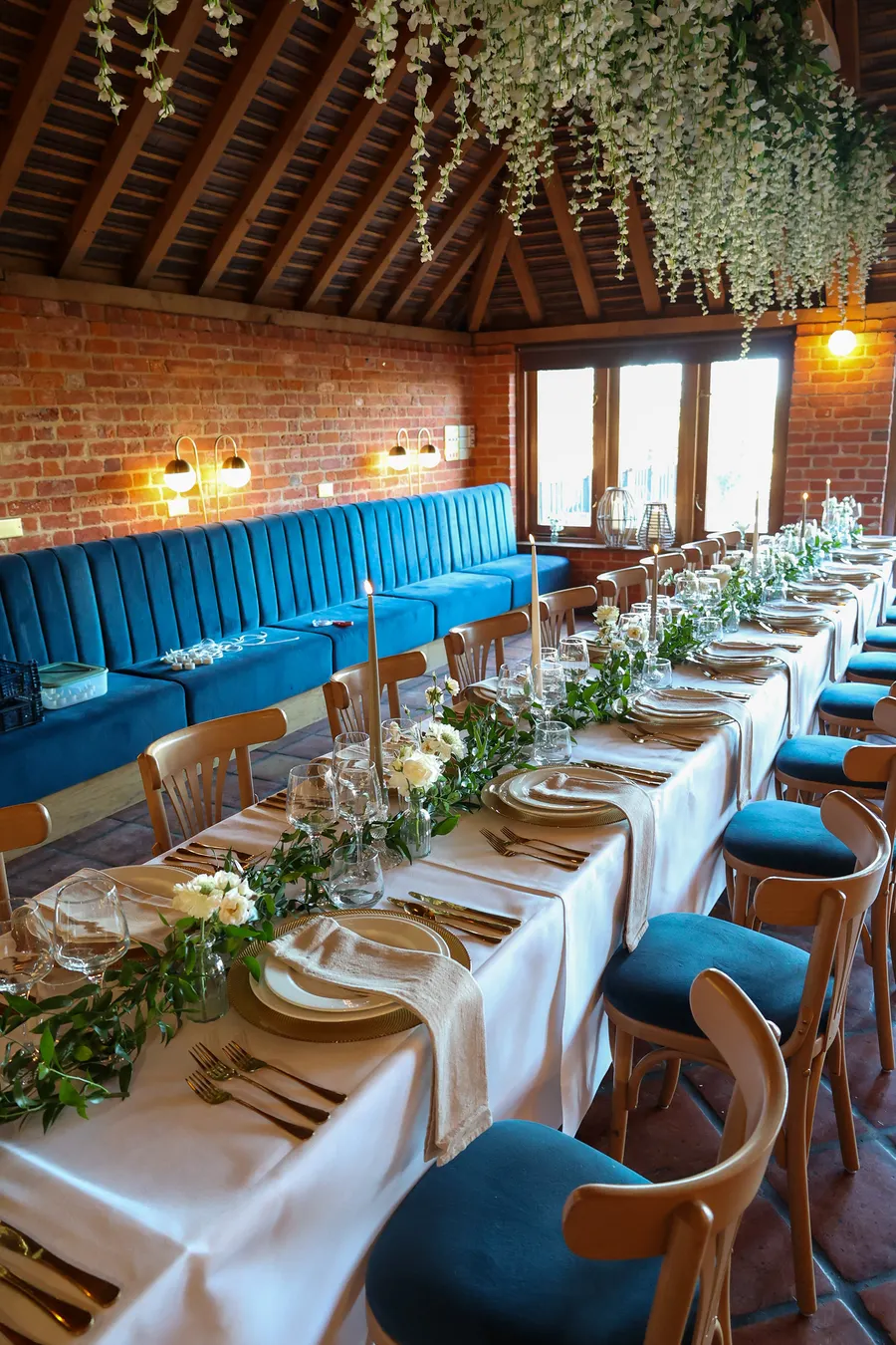 Barn reception table set along a blue banquette beneath hanging foliage