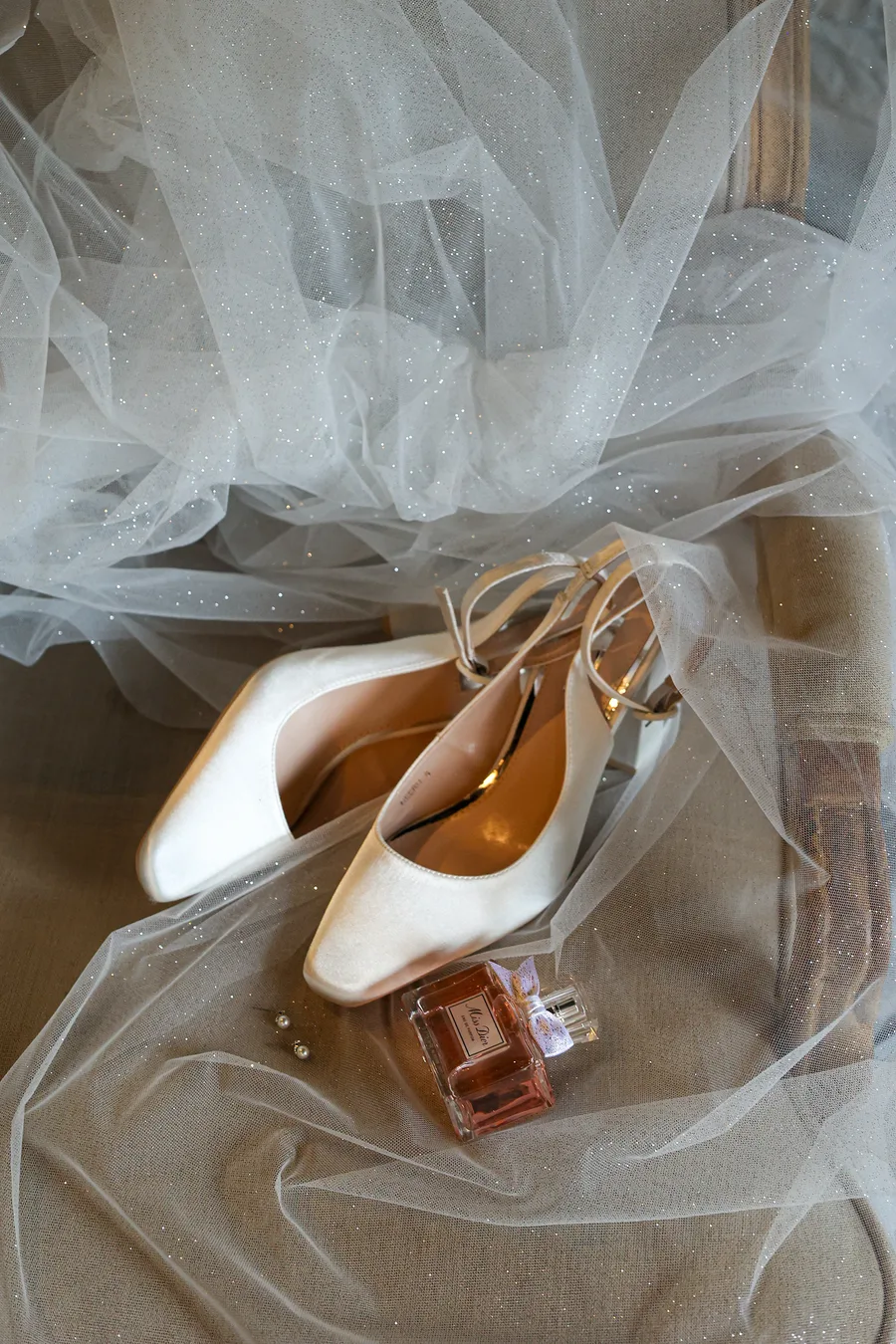 Bridal heels and a bottle of perfume resting on the bride's veil