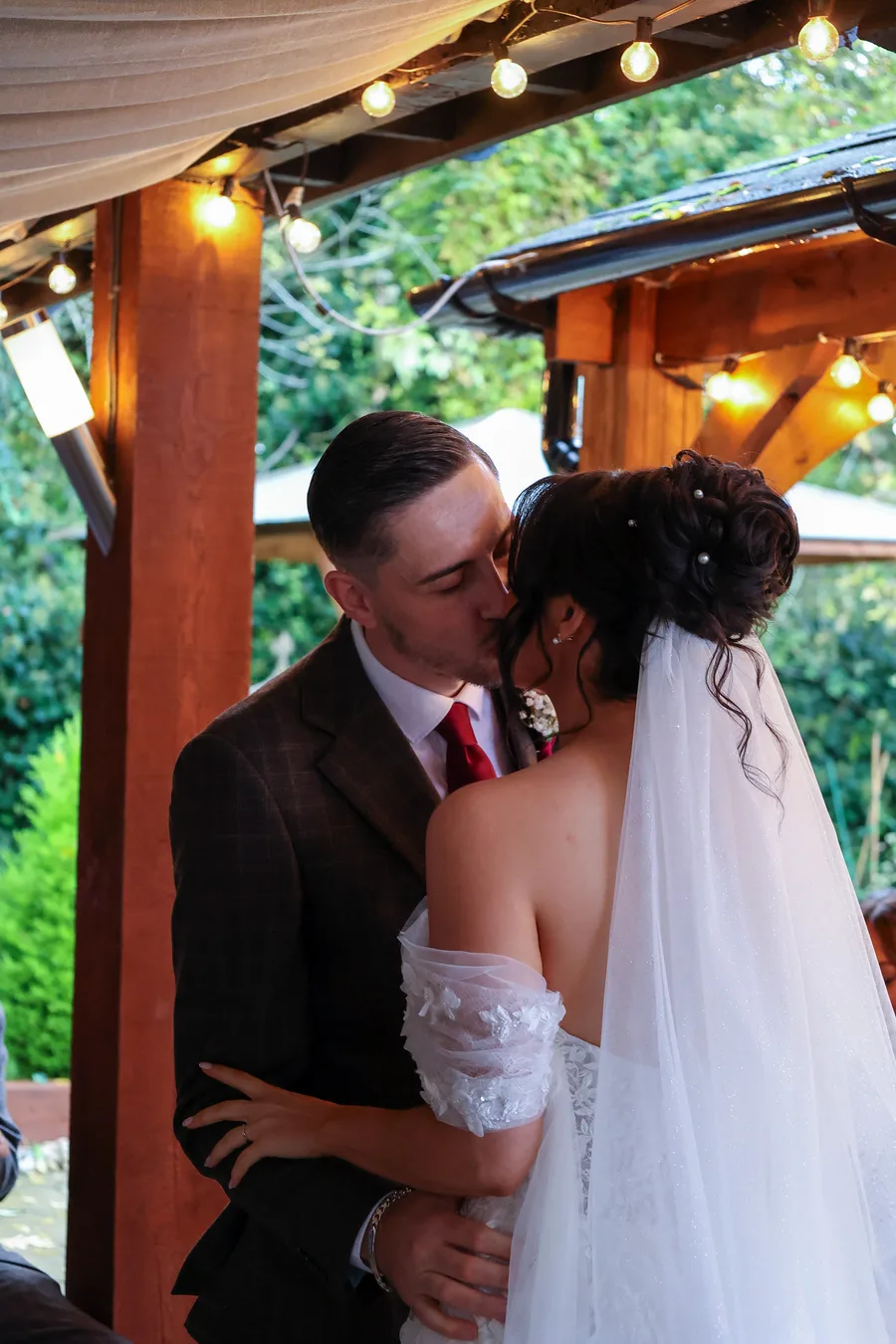 Bride and groom kissing beneath a lit pergola