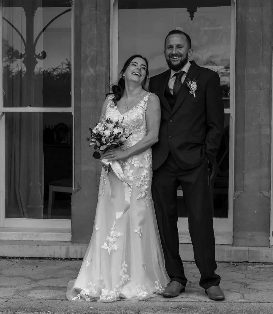 Bride and groom laughing together on the veranda, in black and white