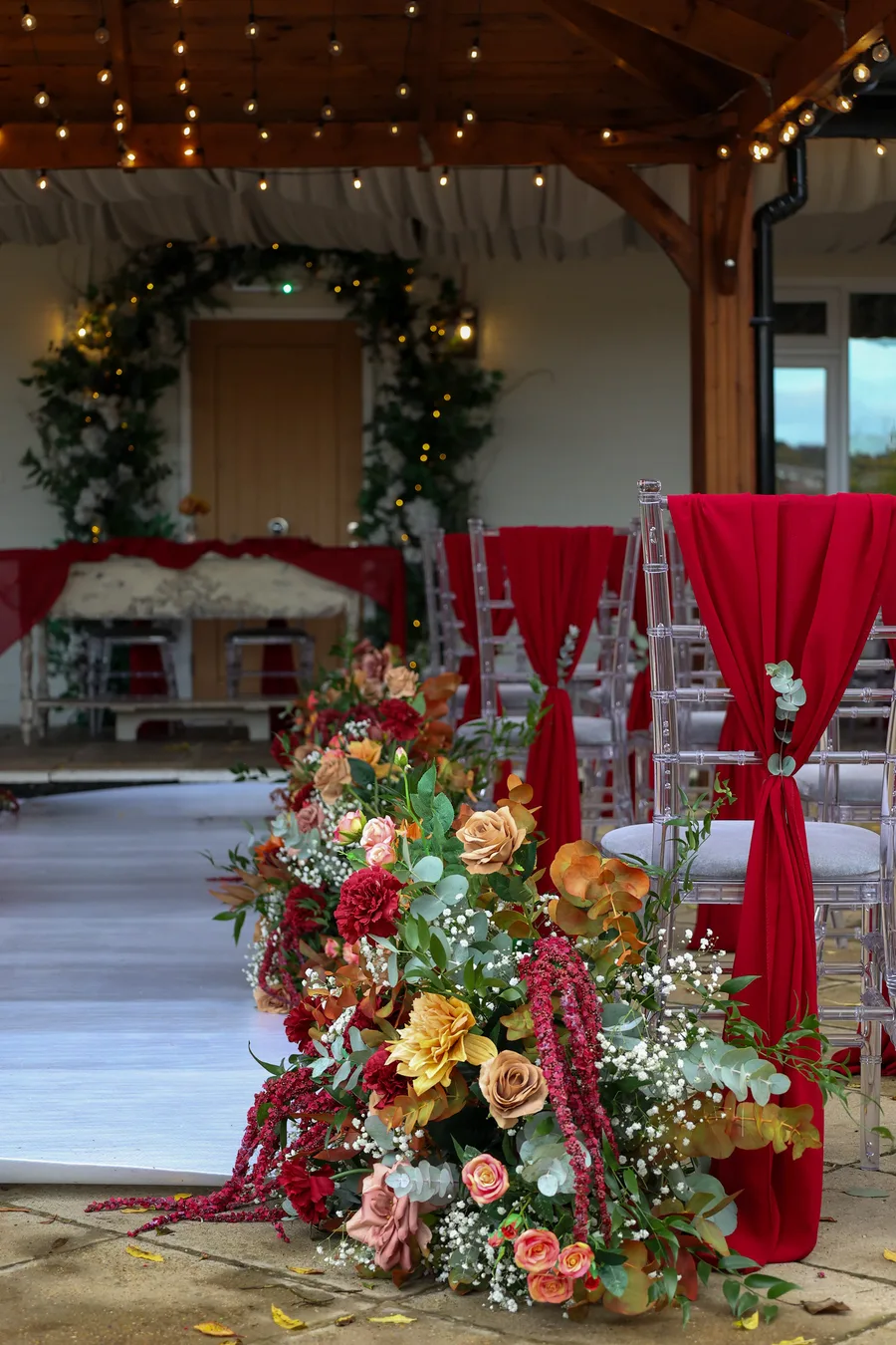 Autumn ceremony flowers in deep red and orange beside the aisle
