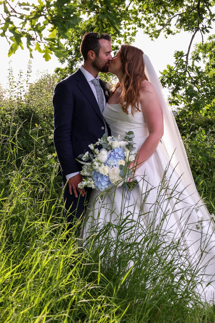 Bride and groom kissing in long grass at golden hour