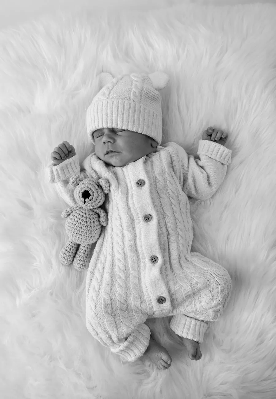 Newborn in a knitted romper and hat with a crochet teddy, in black and white