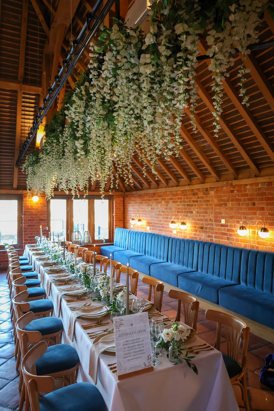 Long table beneath hanging wisteria in a brick and beam barn