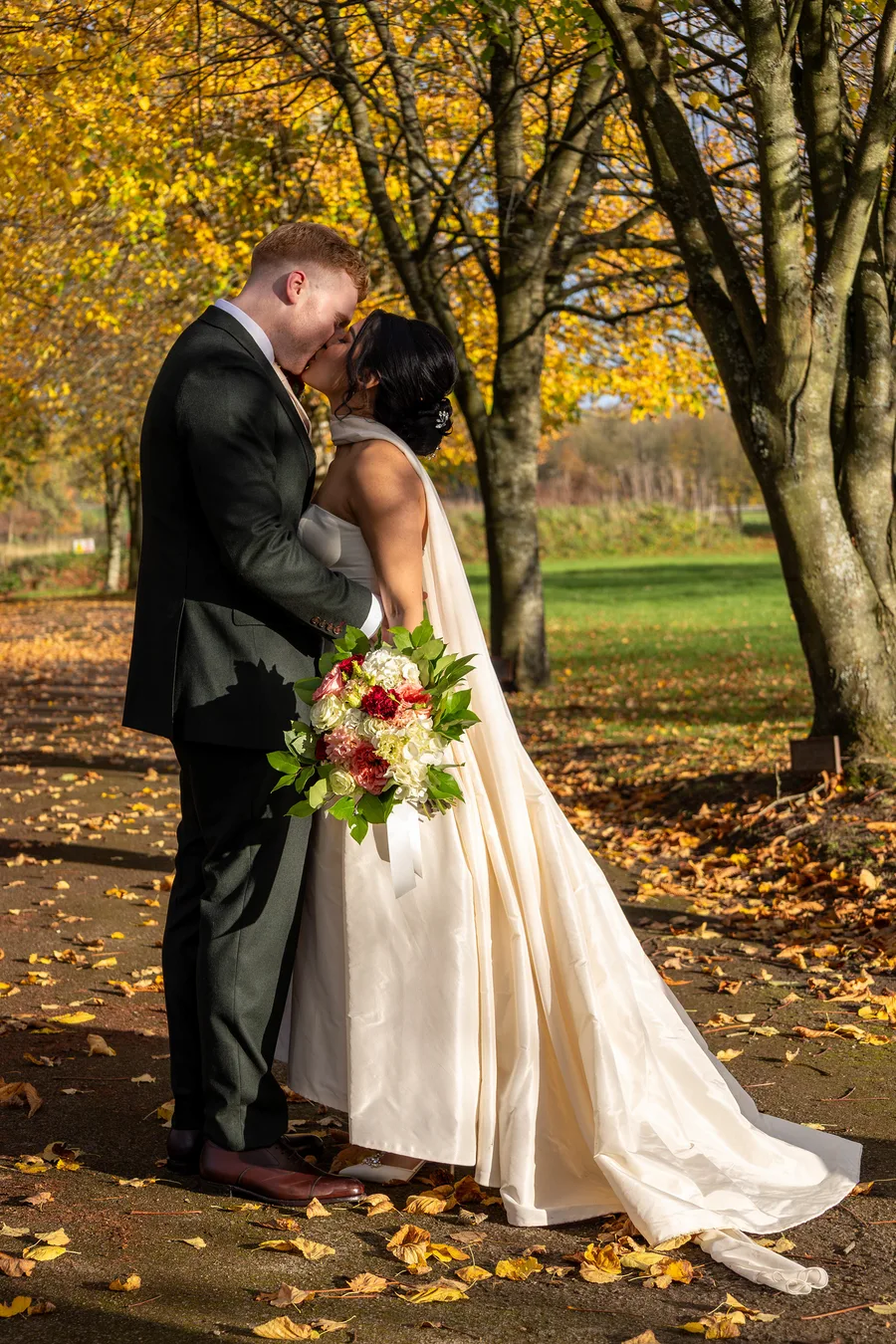 Bride and groom kissing on an avenue of autumn trees