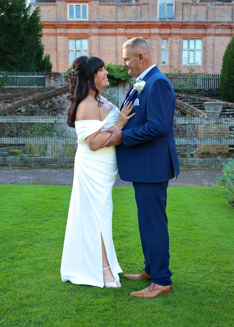 Bride and groom holding each other on the lawn before a red-brick manor