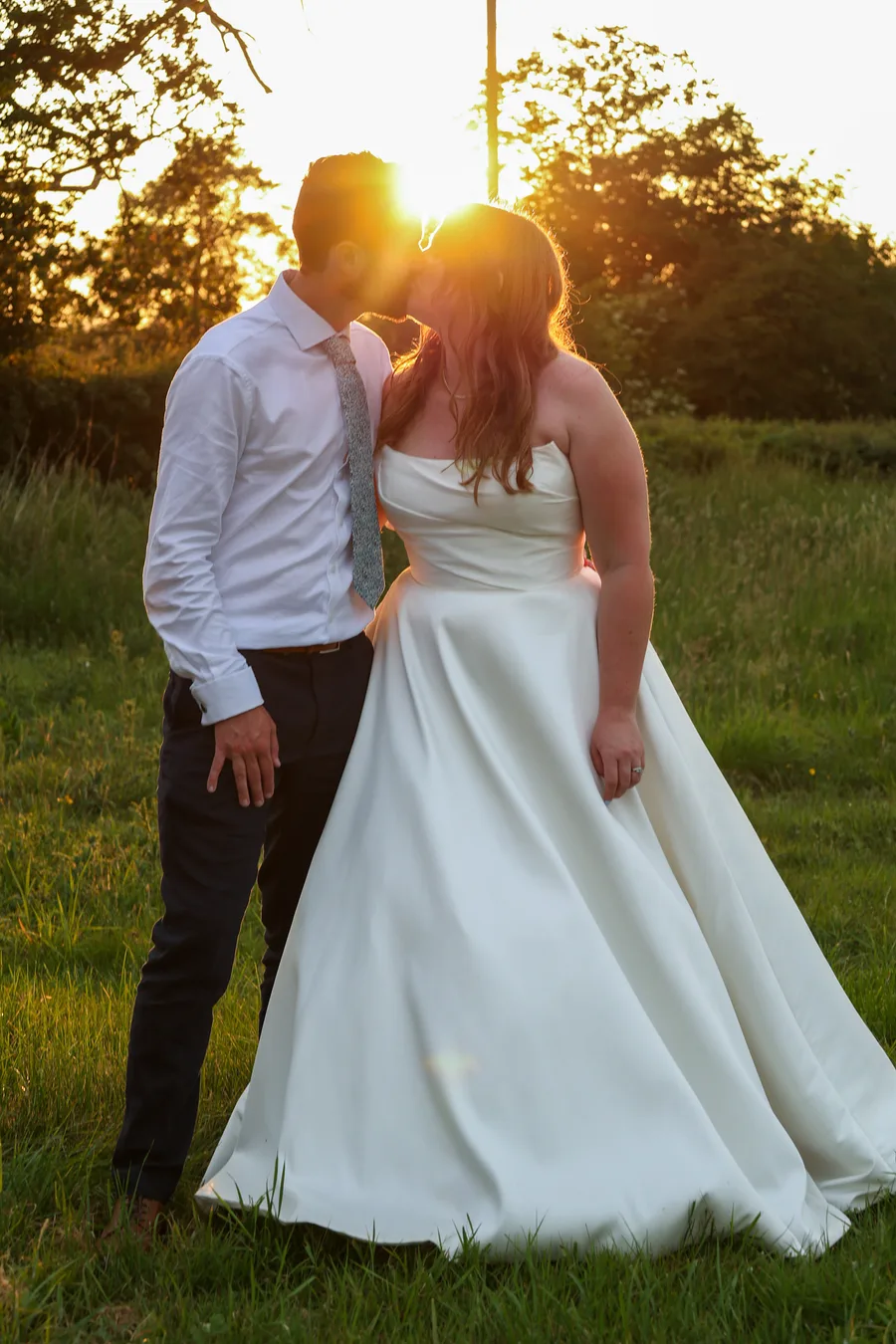Bride and groom kissing with the sun setting behind them