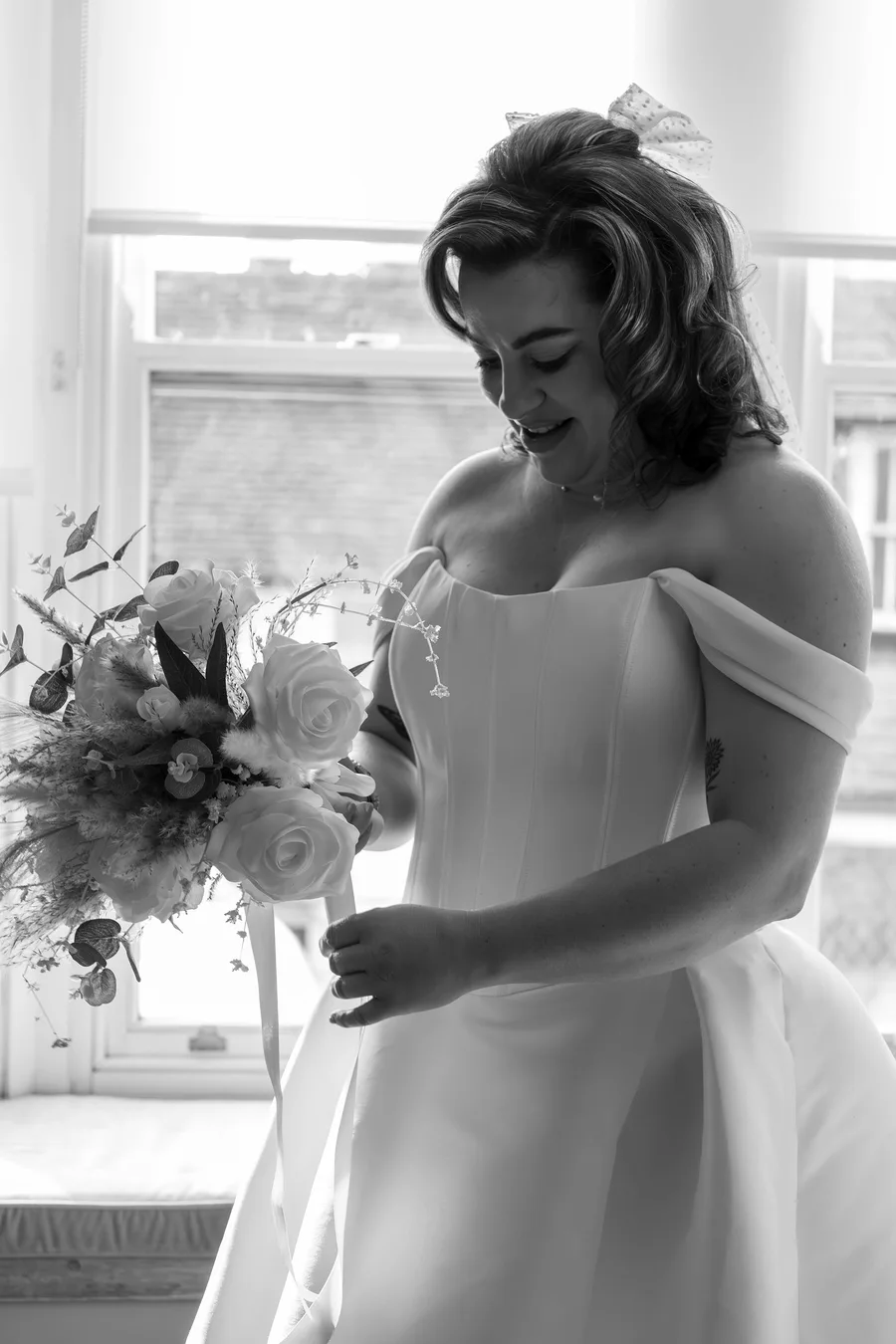 Black and white portrait of the bride holding her bouquet by a window