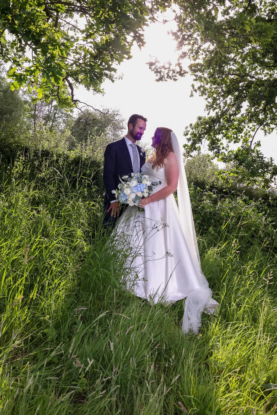 Bride and groom framed by trees in the long grass