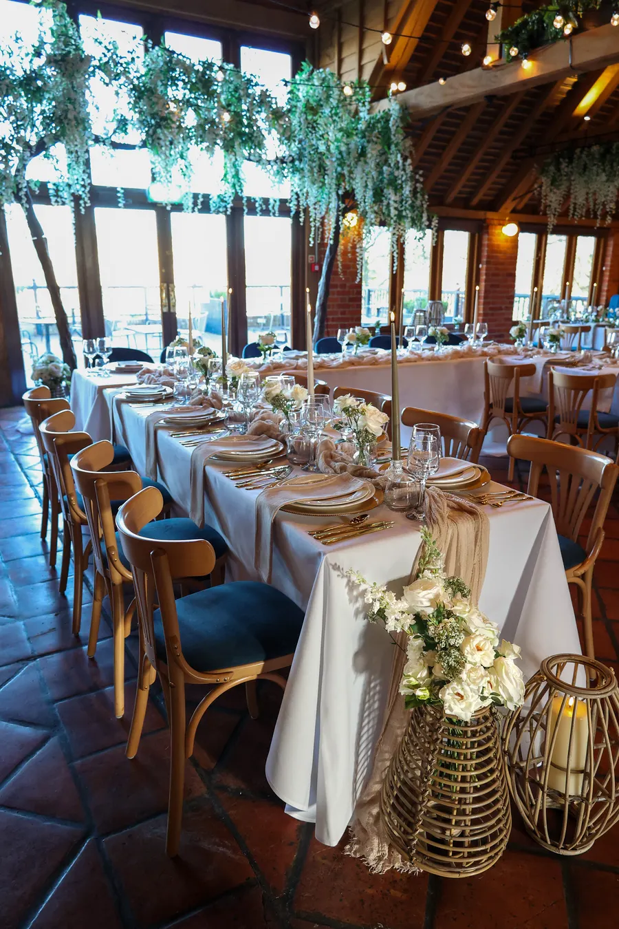 Long banquet table laid with white linen and greenery in a beamed barn