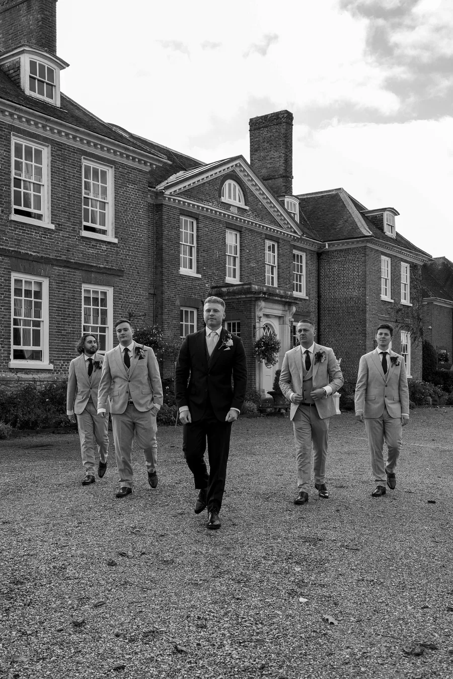 Groom walking up the drive with his groomsmen, in black and white