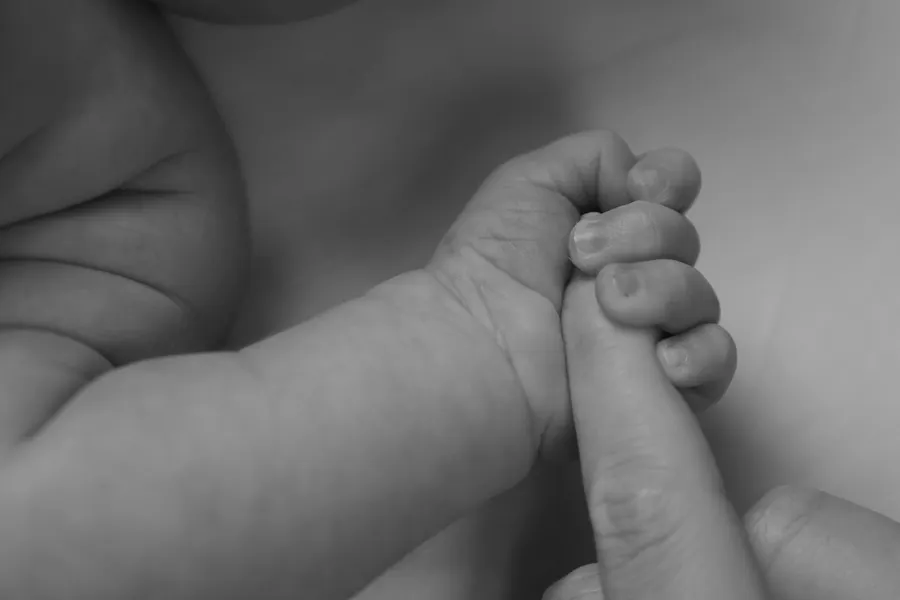 A newborn gripping an adult finger, in black and white