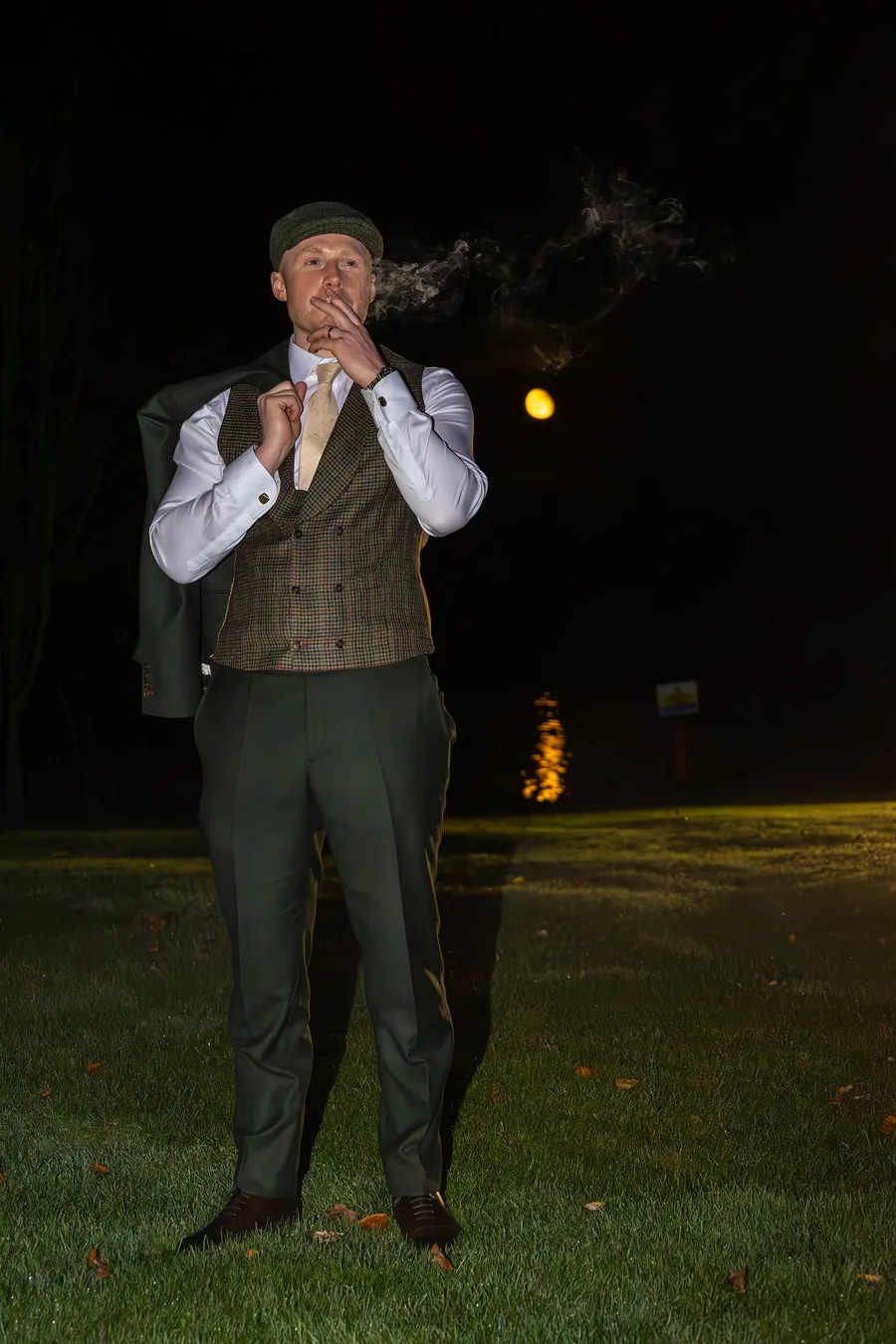 Groom exhaling cigar smoke on the lawn after dark