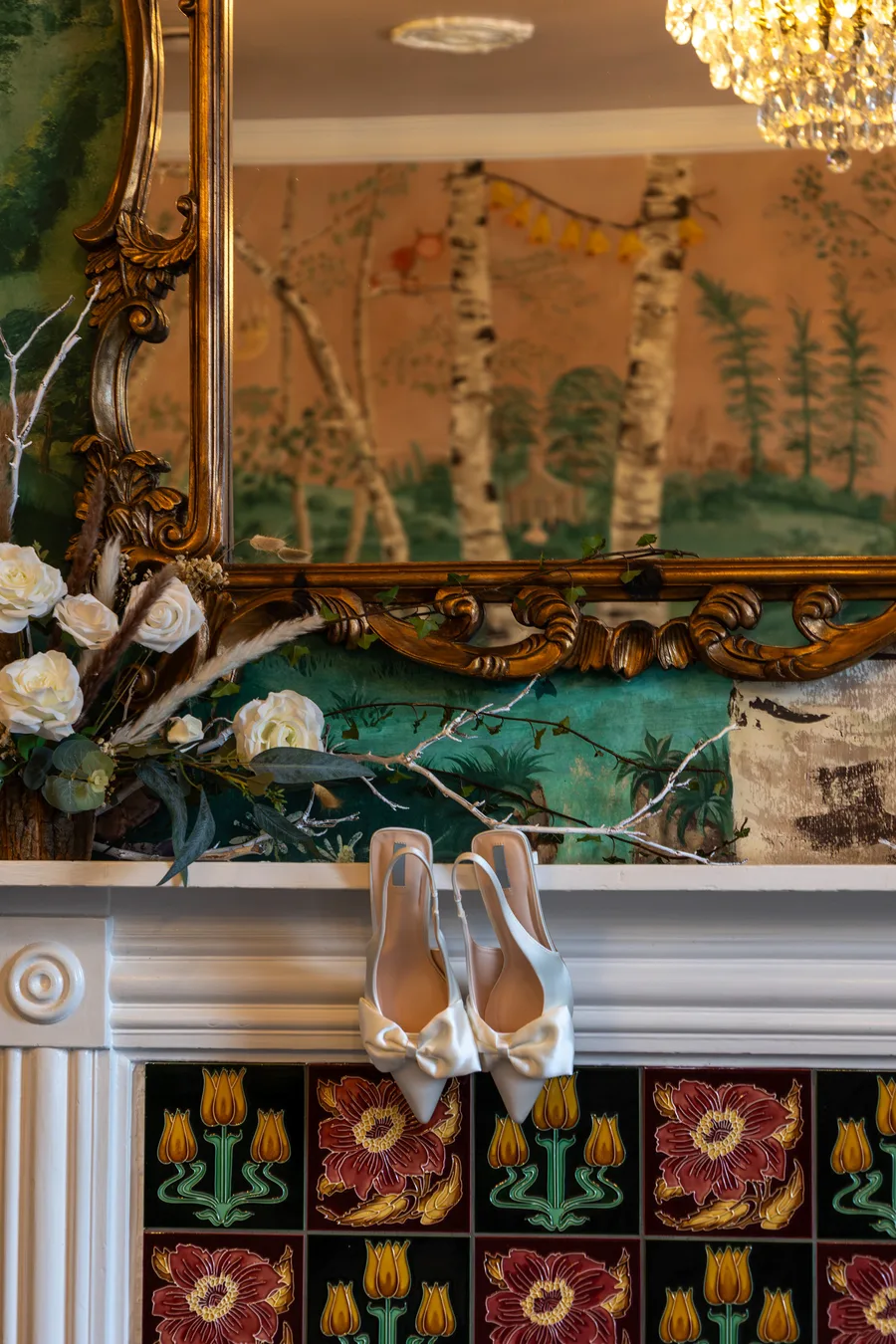 Bridal shoes set on a tiled fireplace beneath a gilded mirror