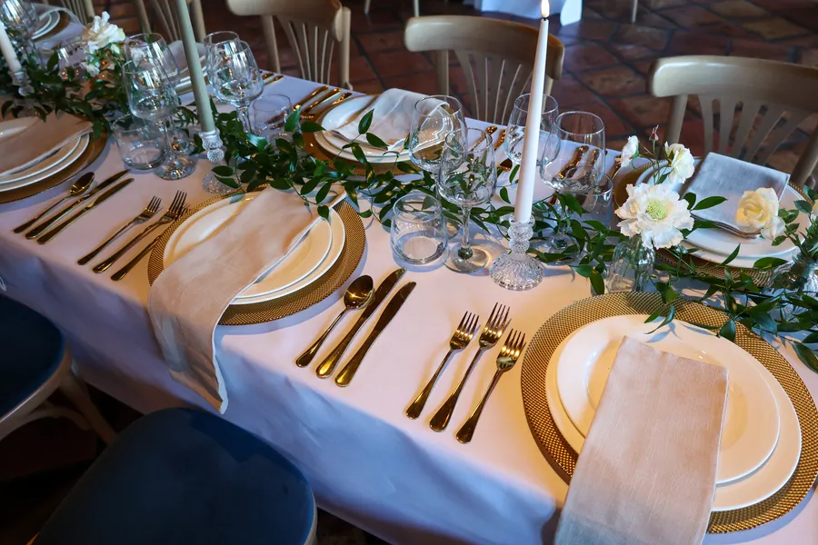 Table laid with gold cutlery, tapered candles and white blooms