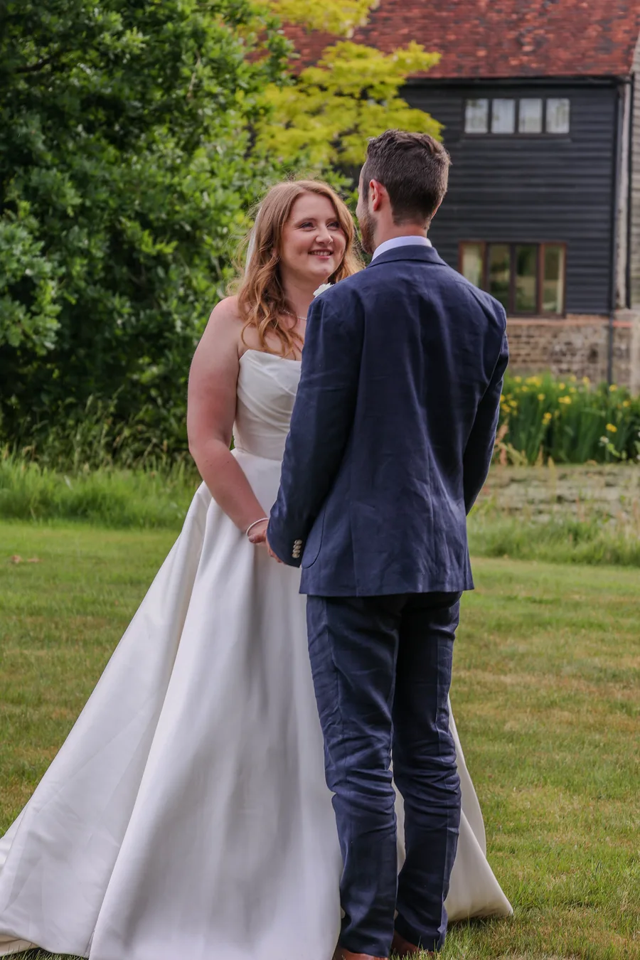 Bride and groom facing each other on the lawn outside a barn venue