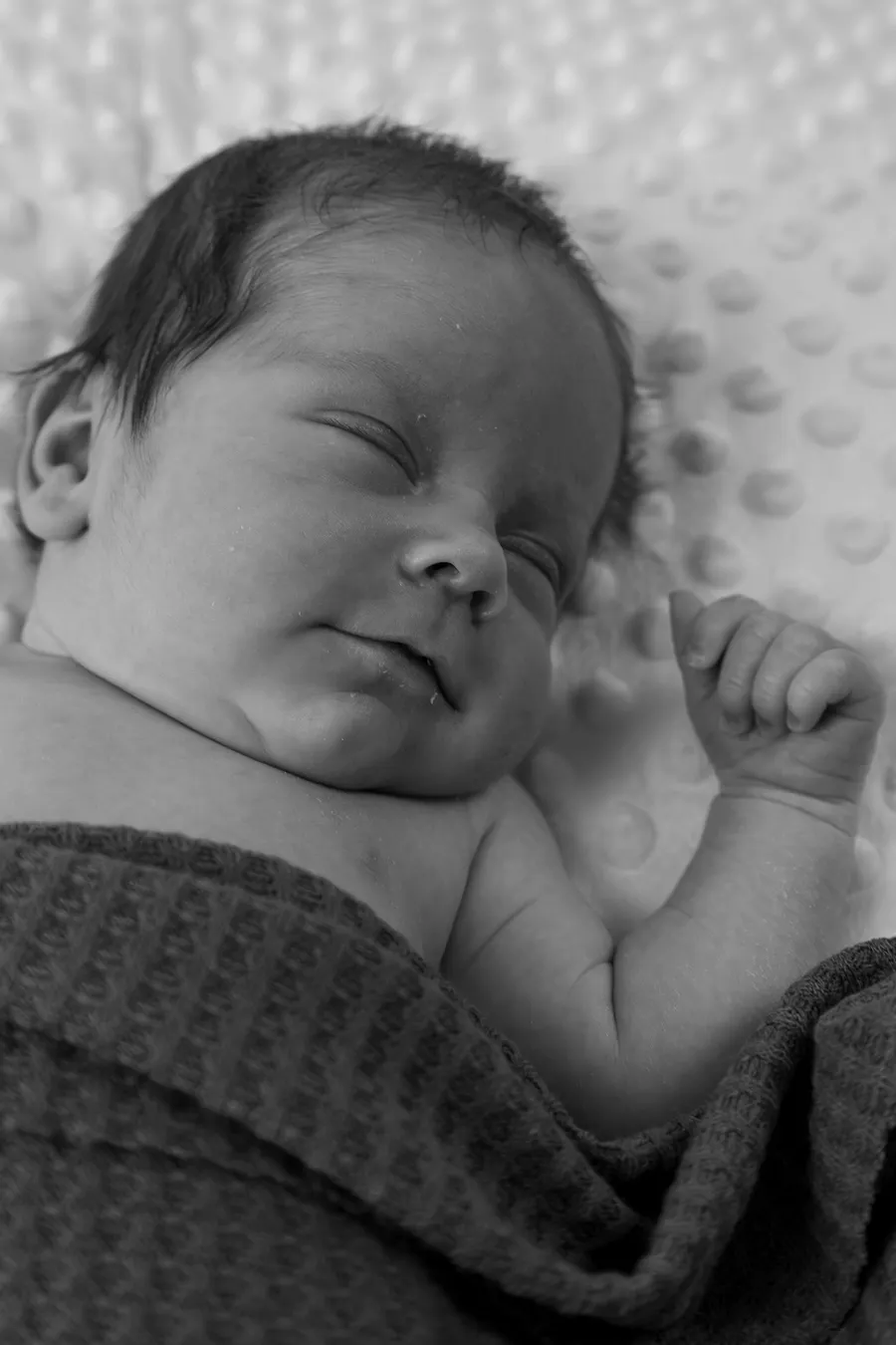 Newborn baby asleep in a waffle blanket, in black and white