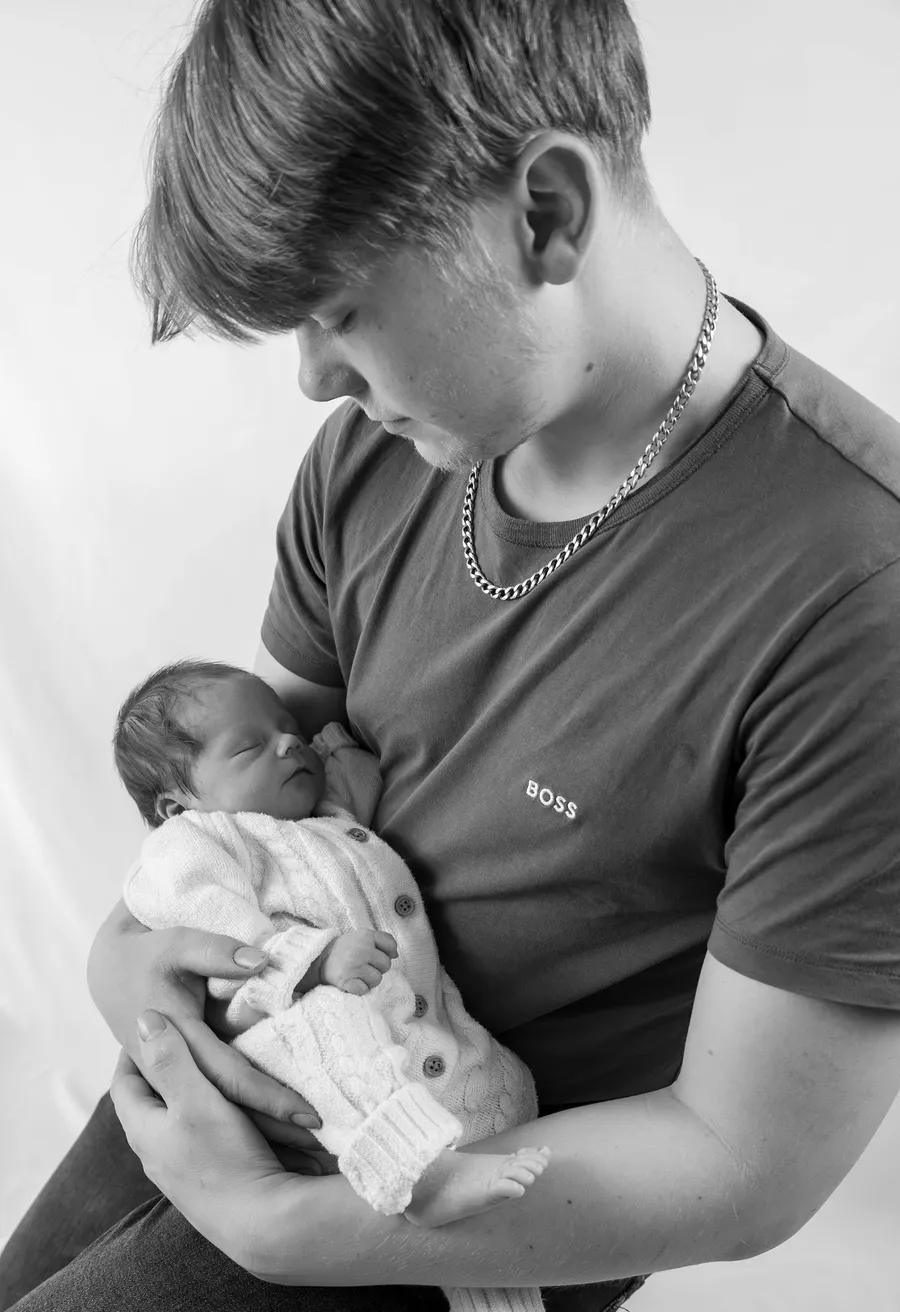 A teenage boy cradling a newborn baby, in black and white