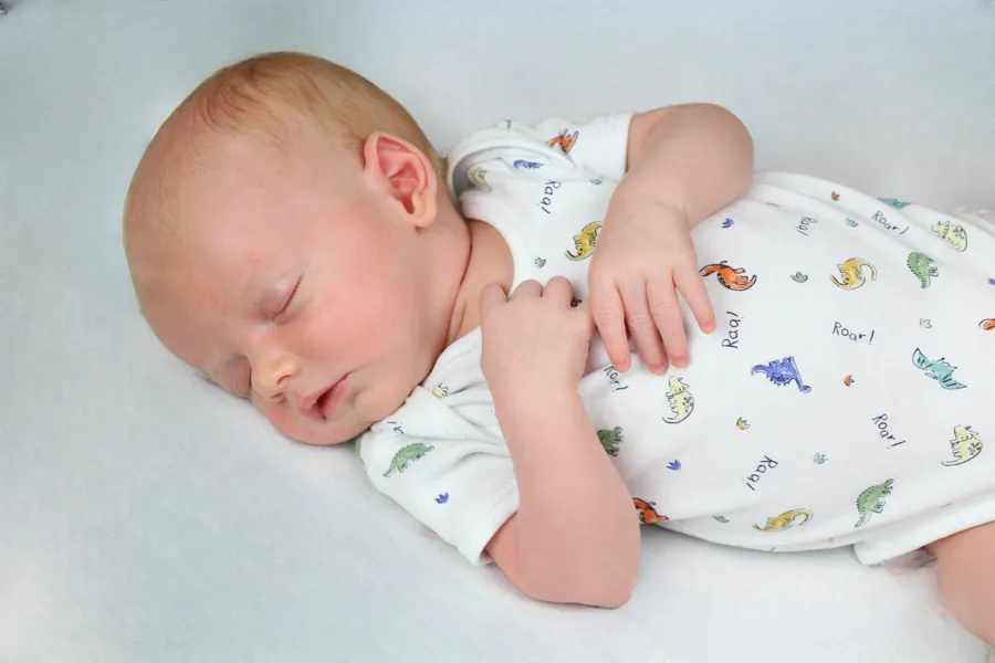 Newborn asleep in a dinosaur-print babygrow