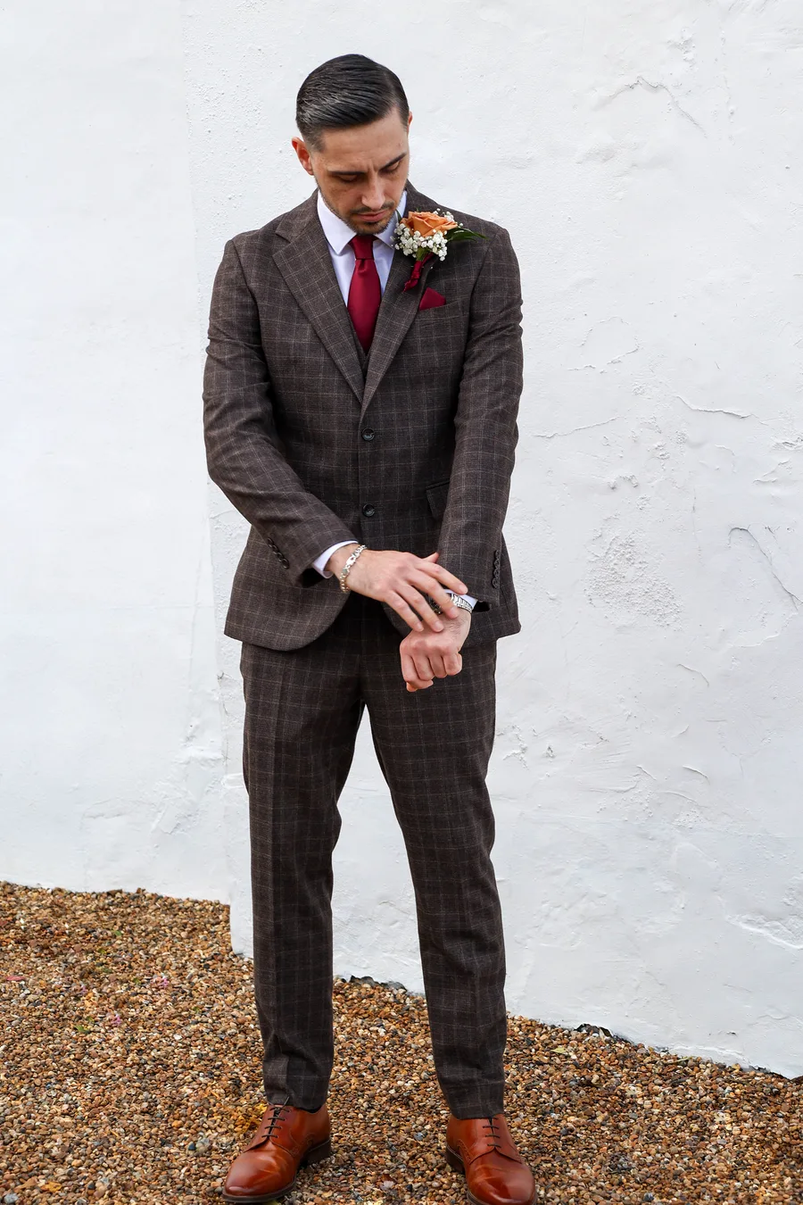 Groom checking his watch outside a white-washed barn
