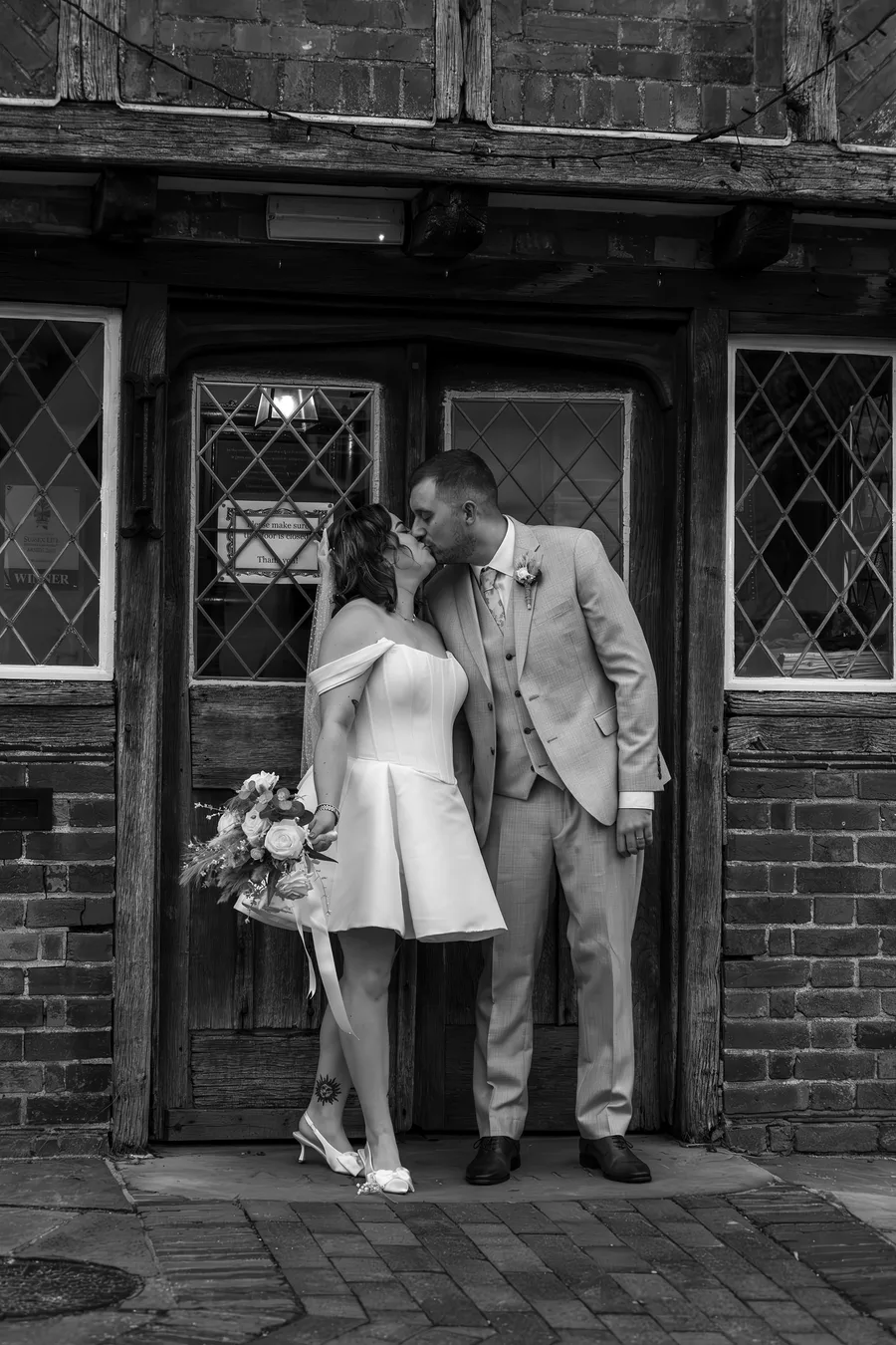 Bride and groom kissing in the doorway of a Tudor timbered building, in black and white