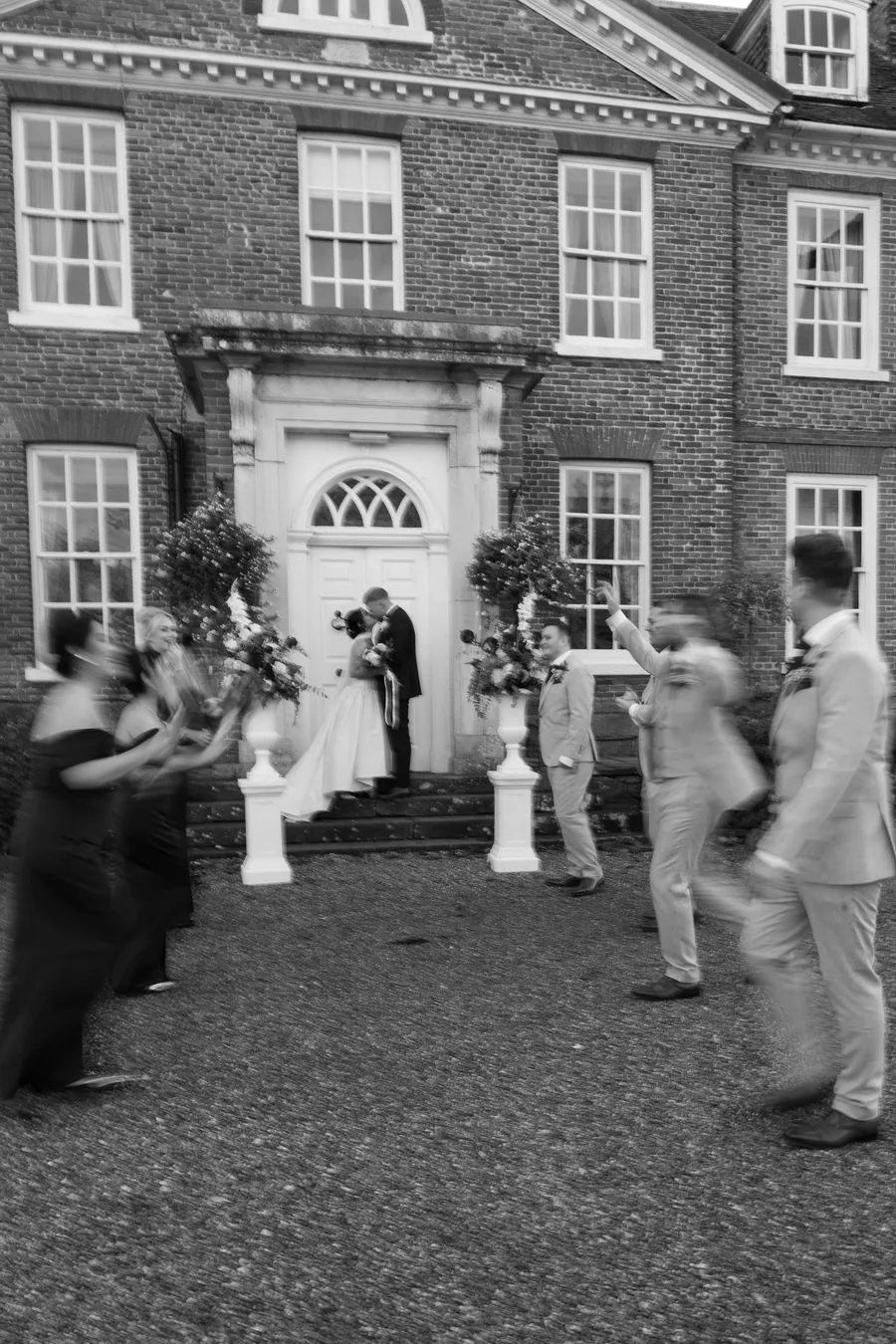 Confetti thrown over the couple outside a Georgian house, in black and white