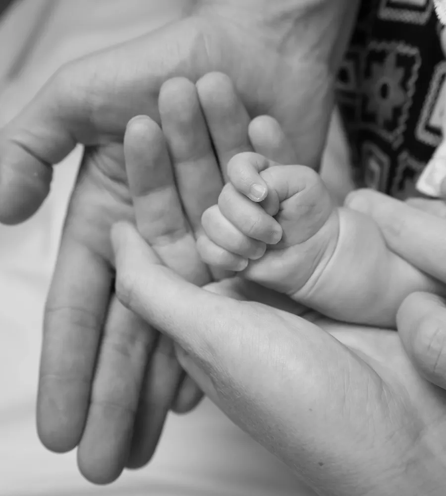 A newborn's hand curled around an adult finger, in black and white