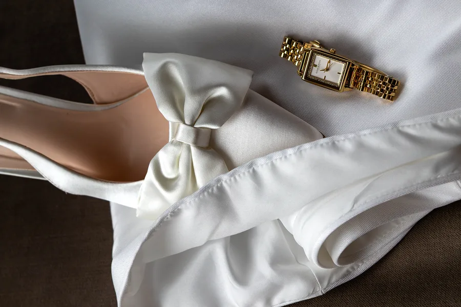 Bridal shoes, a gold watch and dress detail laid out together