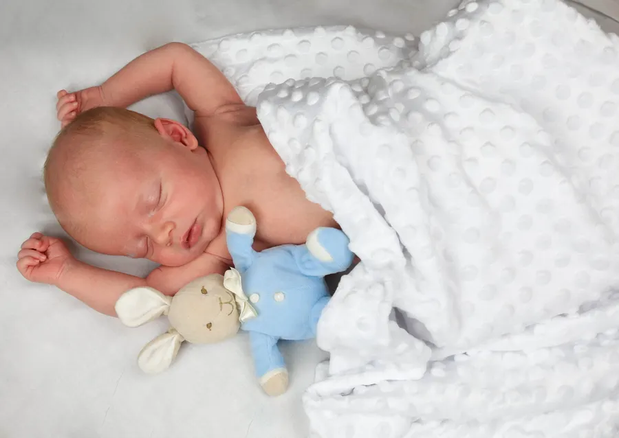 Newborn asleep with a bunny toy and white blanket