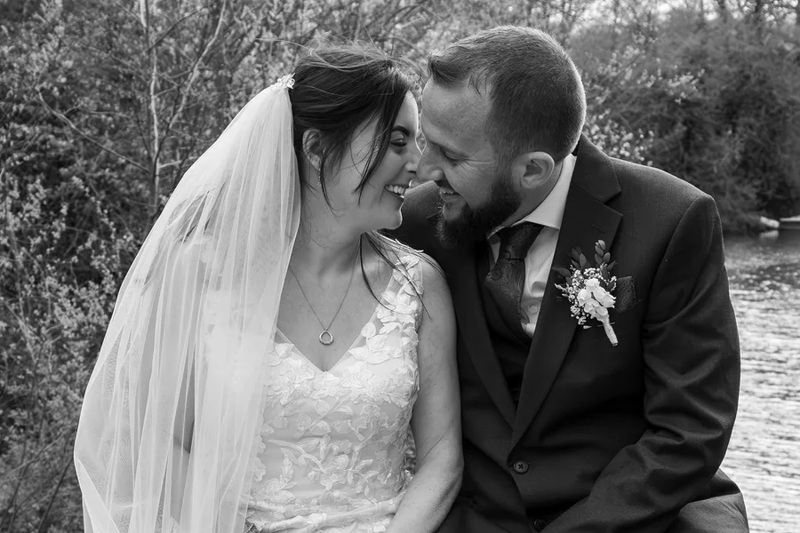 Bride and groom close together by the river, in black and white